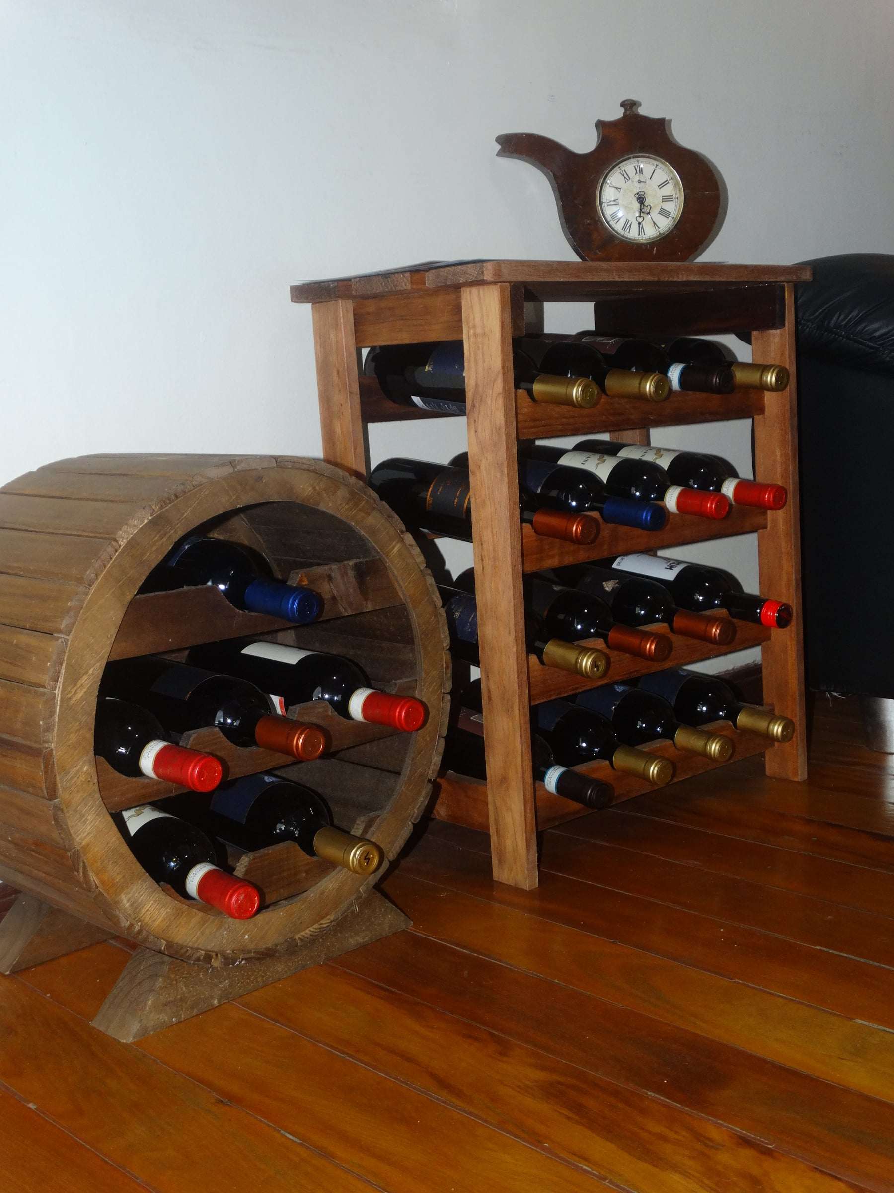 Adega de madeira com garrafas de vinho deitadas num barril e numa estante, sob um relógio