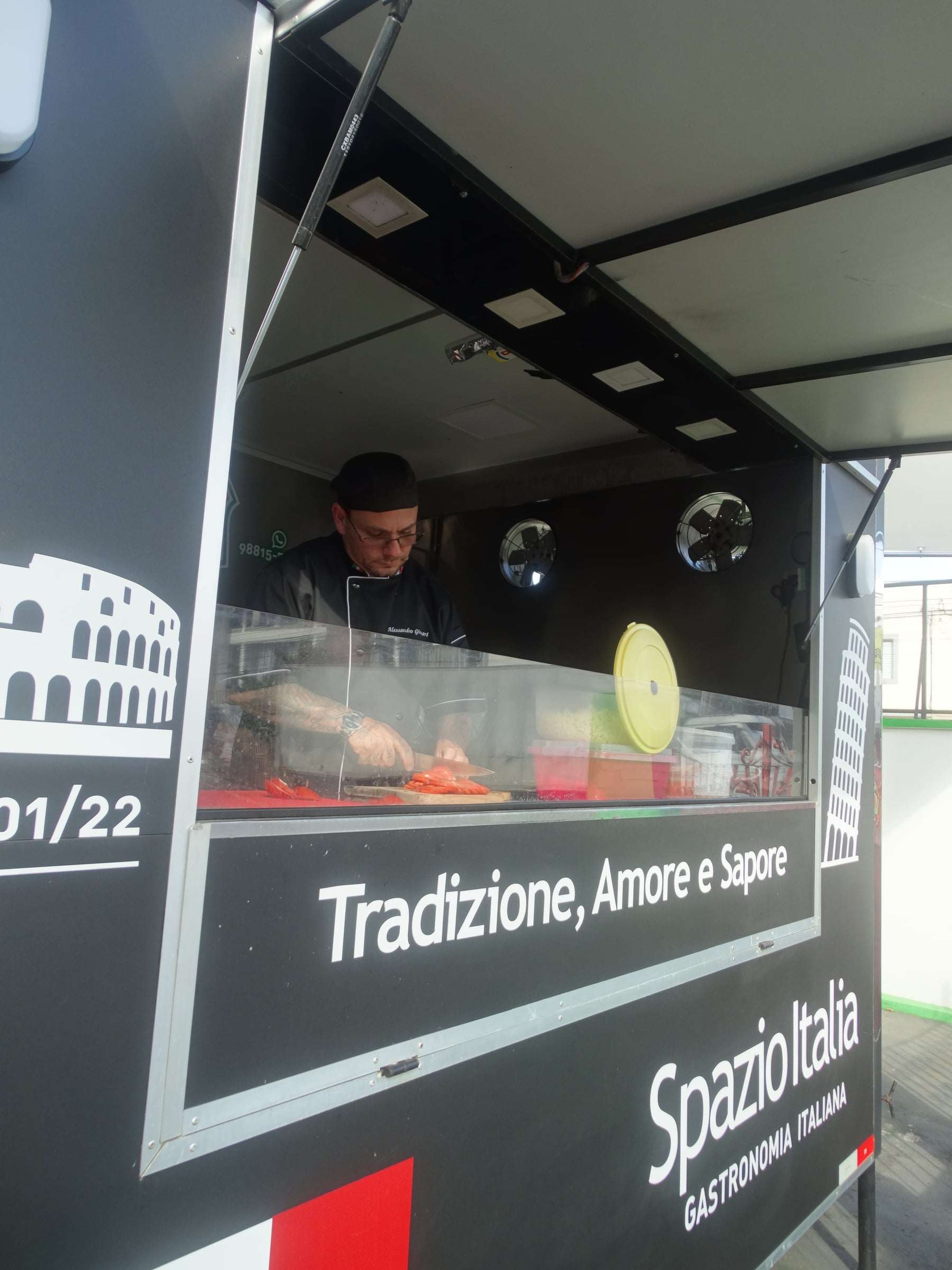 Food truck preto do Spazio Italia aberto, com o chef no balcão e os dizeres Tradizione, Amore e Sapore