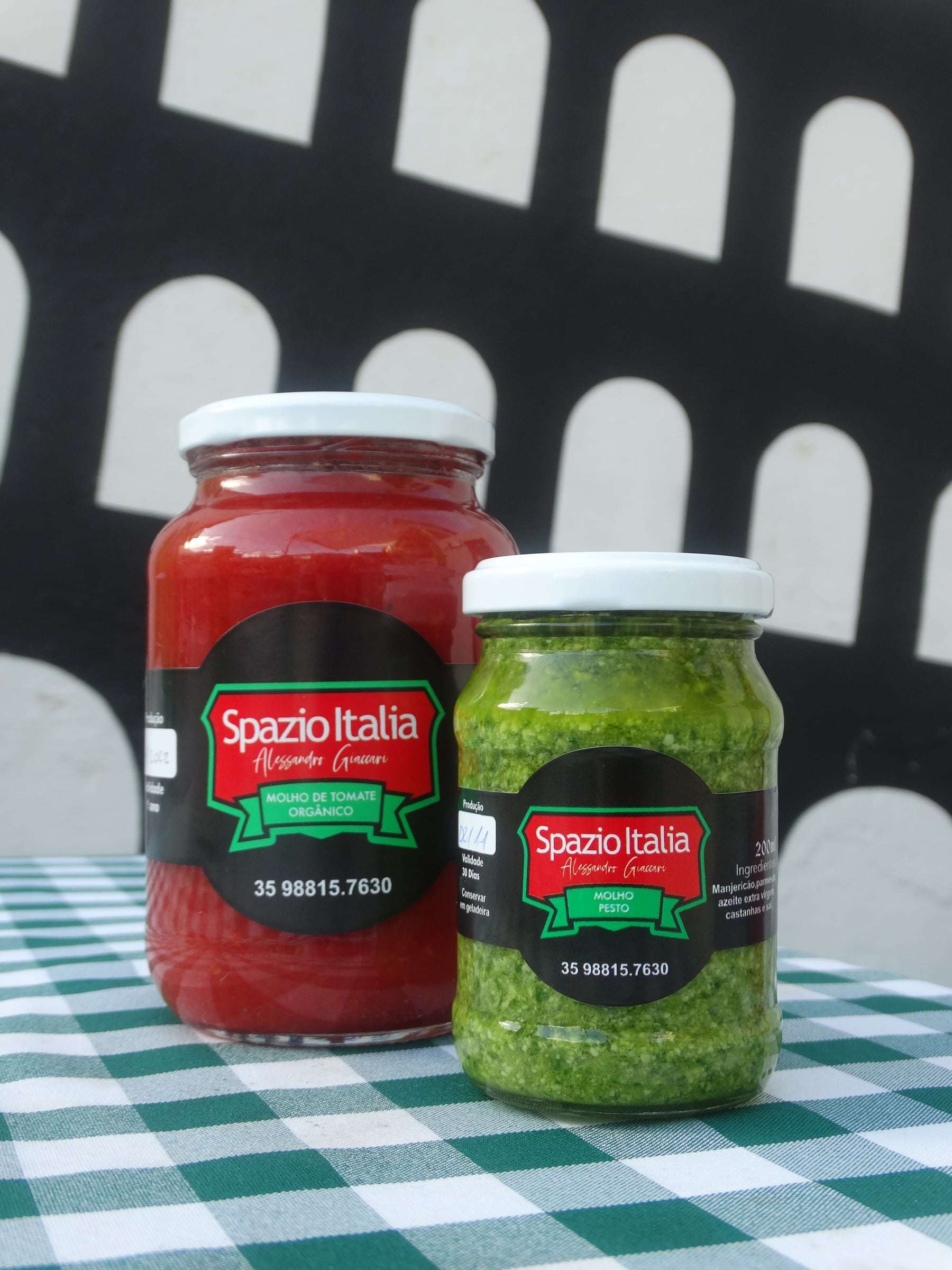 Potes de molho de tomate e de molho pesto do Spazio Italia sobre a toalha xadrez, diante do mural do Coliseu