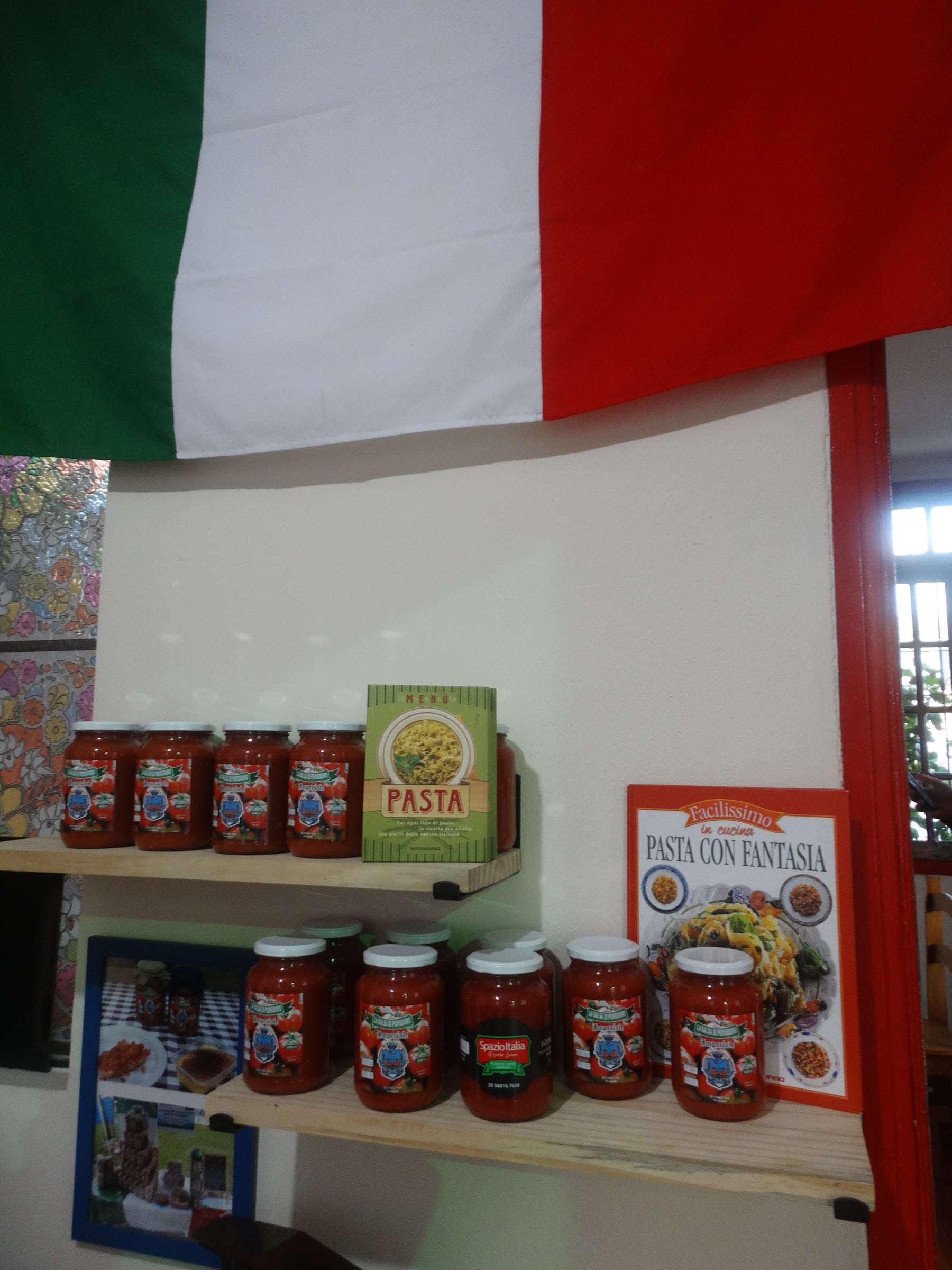 Prateleiras com potes de molho de tomate, livros de receitas de massa e a bandeira da Itália acima
