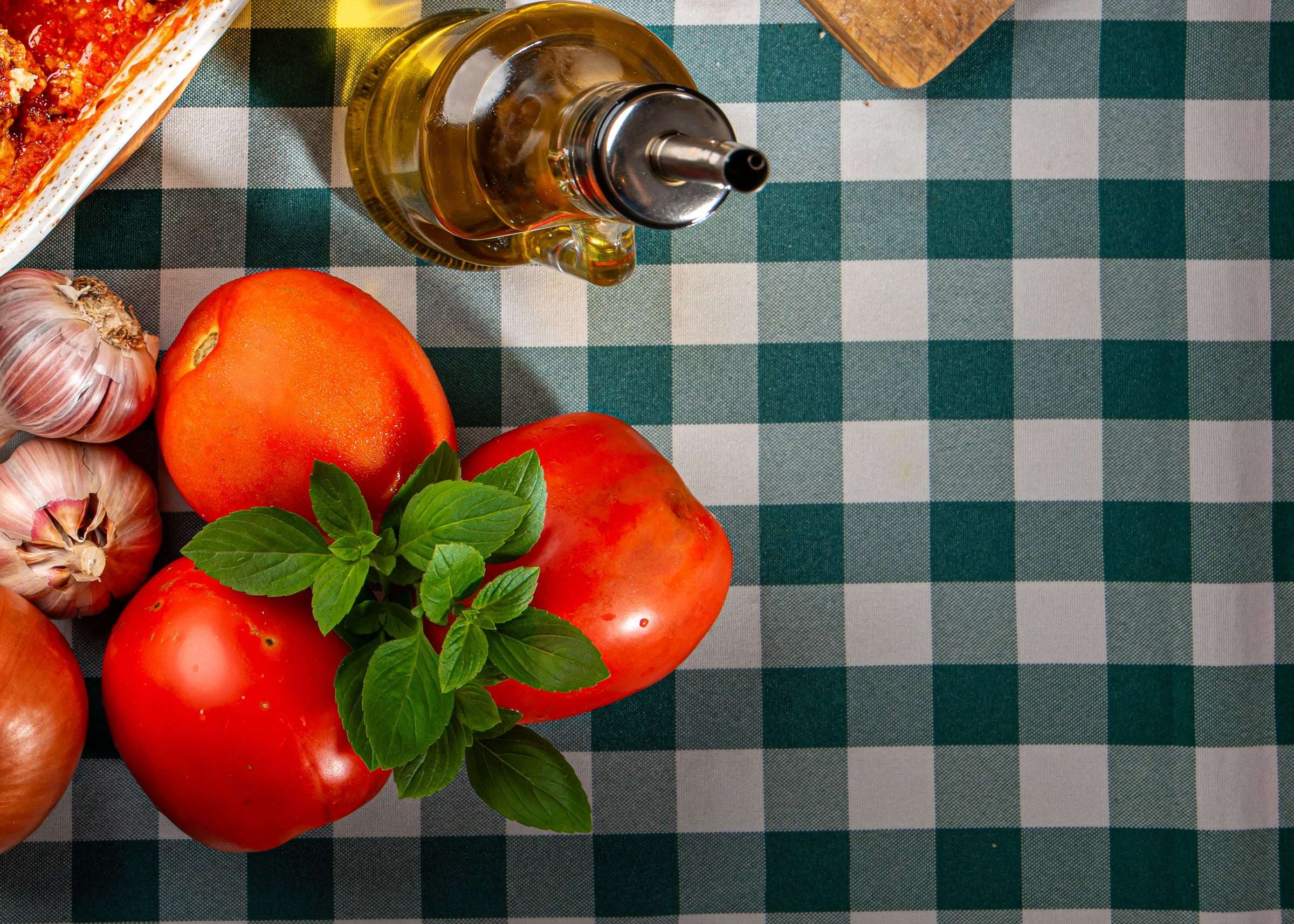 Tomates, manjericão, alho, cebola e azeite sobre a toalha xadrez verde e branca